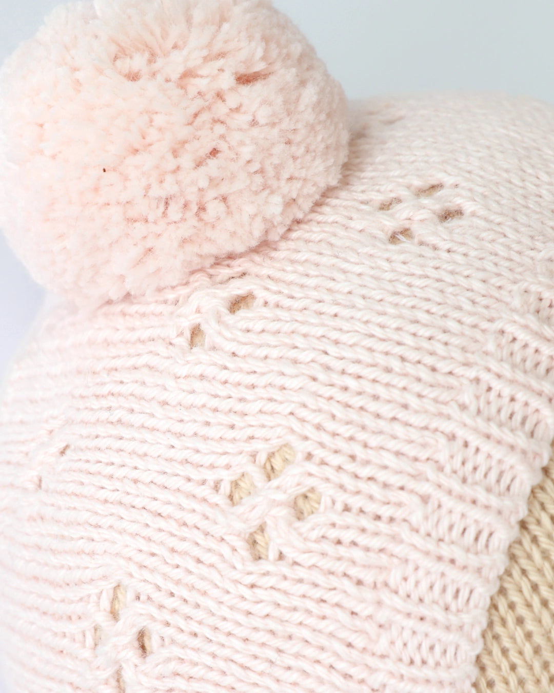 Close-up of a pink knitted hat with a pom-pom on a light background