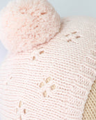 Close-up of a pink knitted hat with a pom-pom on a light background
