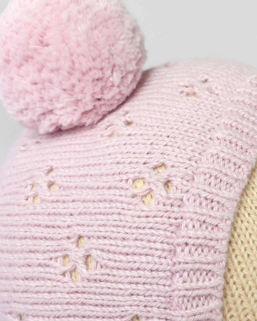 Close-up of a pink knitted item with a fluffy pink pom-pom on a light gray background.