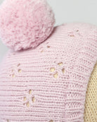 Close-up of a pink knitted item with a fluffy pink pom-pom on a light gray background.