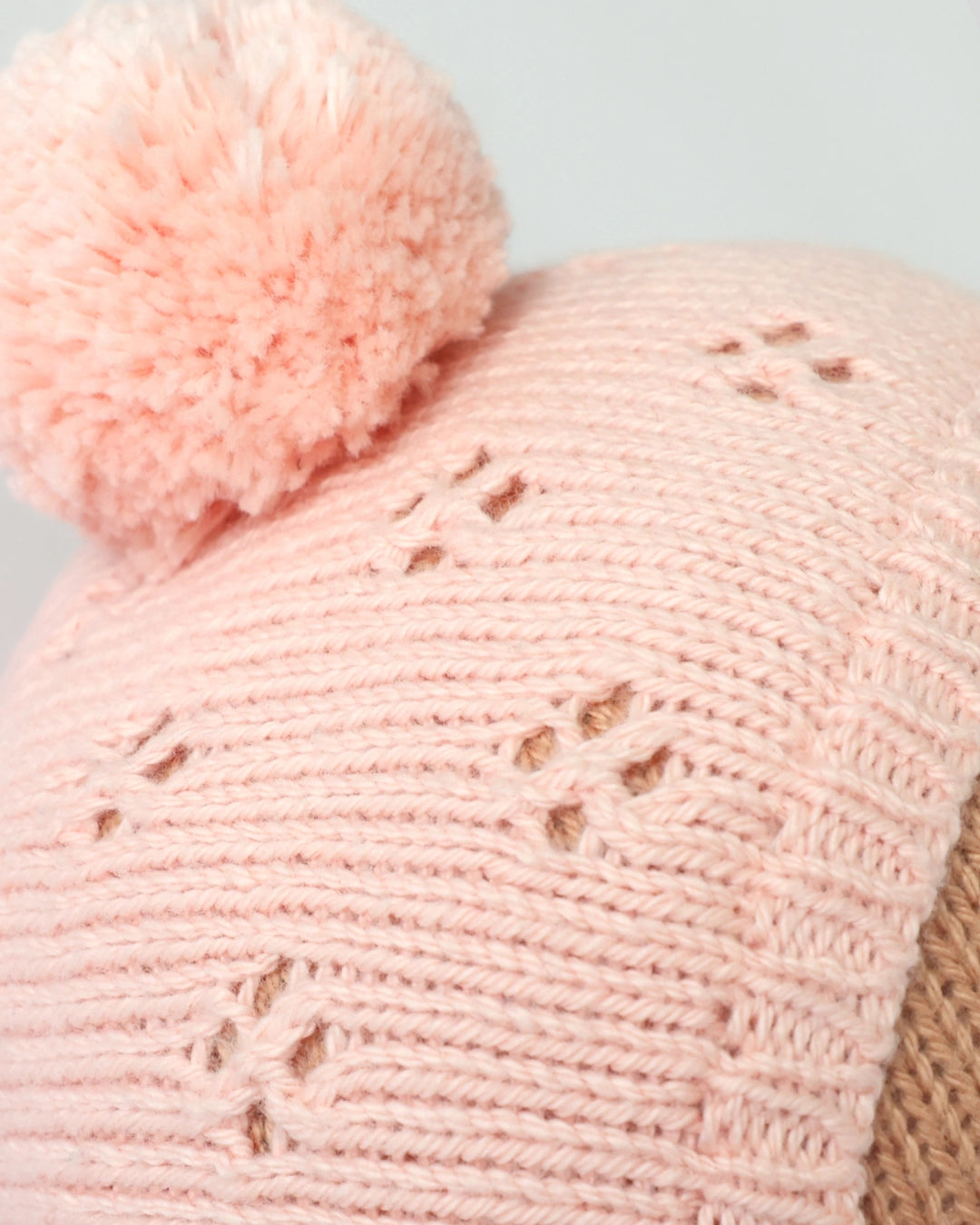 Close-up of a pink knitted hat with a pom-pom on a light gray background