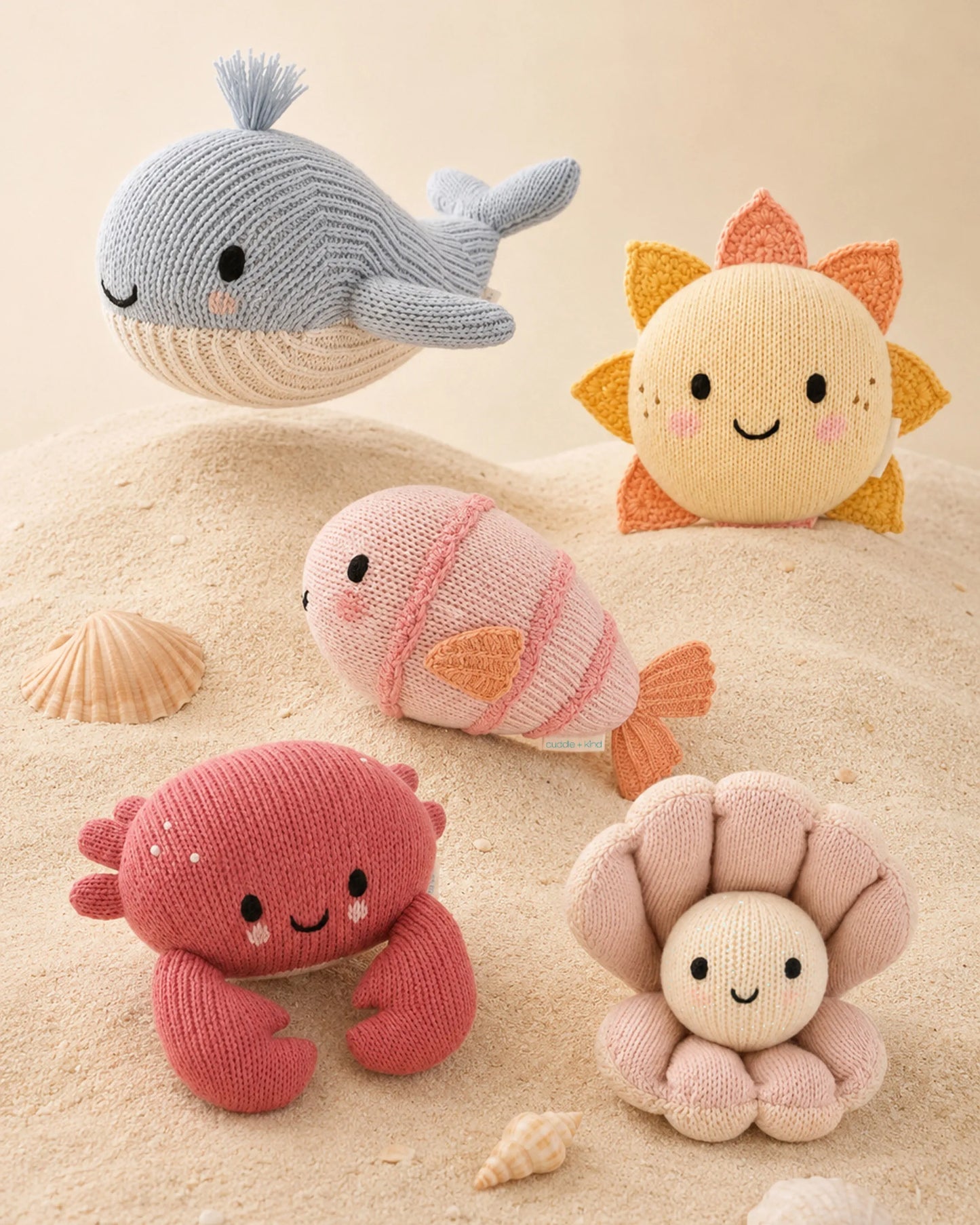 Set of knitted sea-themed toys including a whale, fish, crab, and starfish on a sandy background.