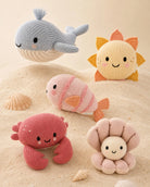 Set of knitted sea-themed toys including a whale, fish, crab, and starfish on a sandy background.