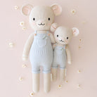 Two knitted teddy bears wearing light blue overalls on a soft pink background with small white flowers.