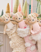 Three teddy bears in dresses sitting on a textured surface with decorative trees in the background.
