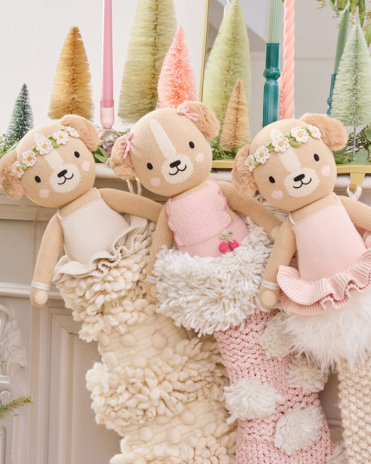 Three teddy bears in dresses sitting on a textured surface with decorative trees in the background.