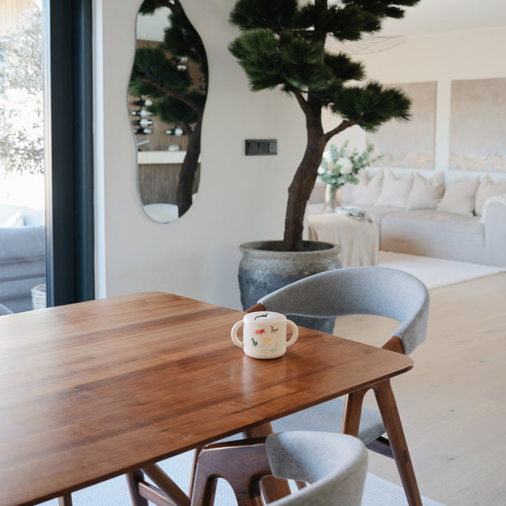 Dining area with wooden table, gray chairs, and a potted plant in a modern living room.