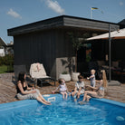 People by a pool with a dark wooden shed and outdoor furniture in the background