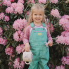 Young girl in teal overalls standing among pink flowers