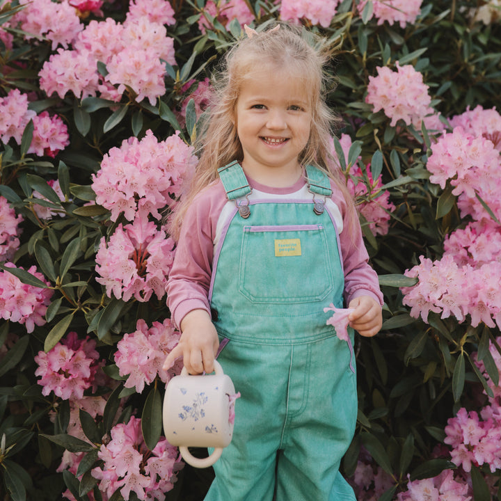 Young girl in teal overalls standing among pink flowers