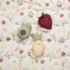 Plush toys shaped like an avocado, strawberry, and pineapple on a fabric with vegetable pattern