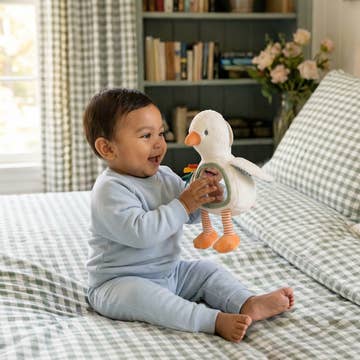 Baby playing with a toy duck on a bed in a home setting