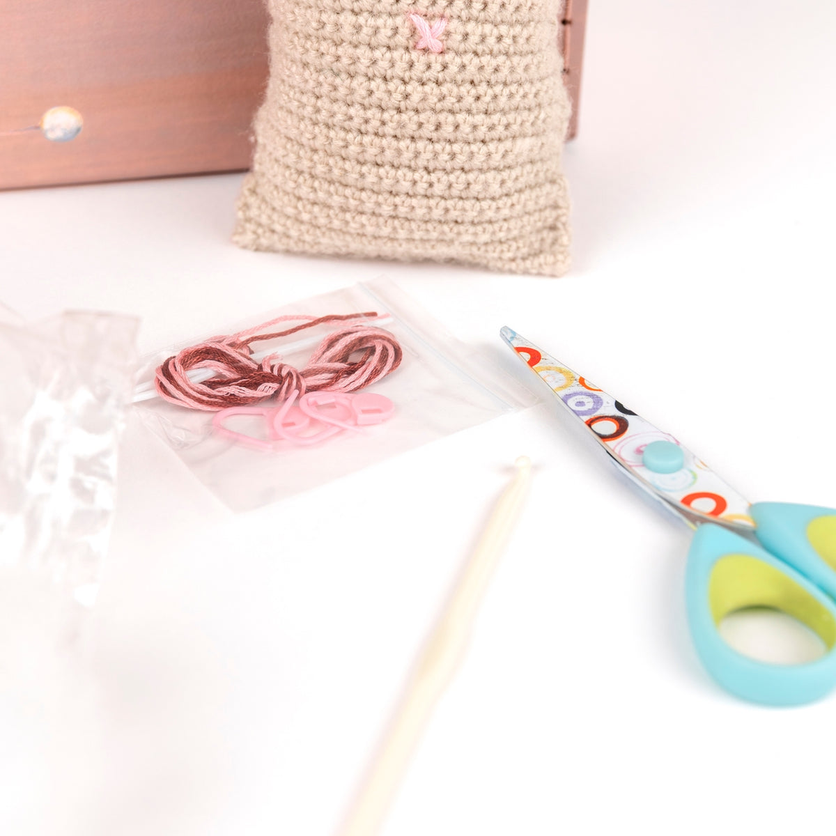 Crochet hook, yarn, and colorful scissors on a white surface