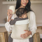 Woman holding a baby in a carrier and a mug indoors