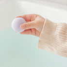 Hand holding a purple bath bomb against a light background