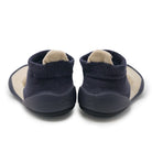 A pair of slip-on baby booties shown from the back, featuring navy blue knit socks with a beige inner lining and a matching navy blue flexible sole.