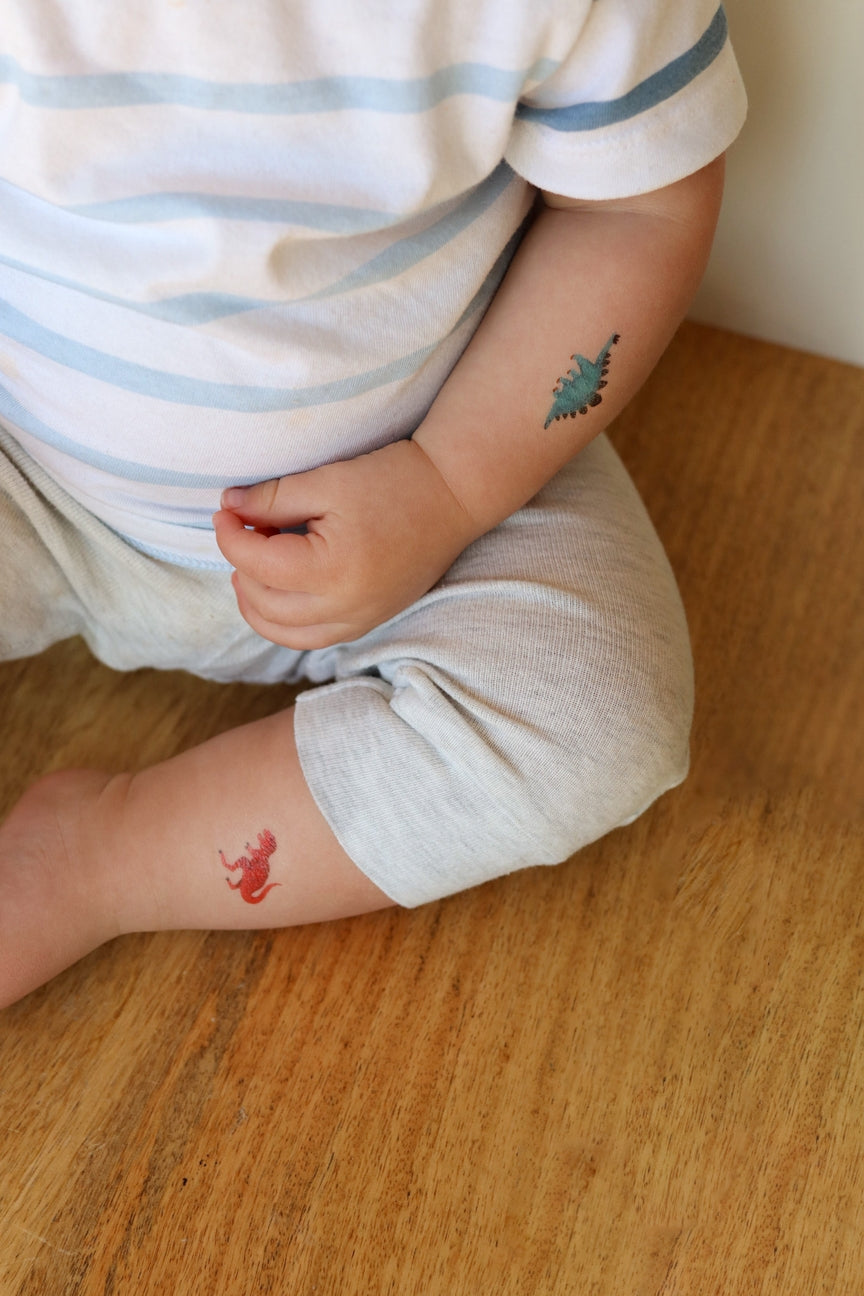 Child with temporary tattoos of a red dragon and a green dinosaur on a wooden floor.