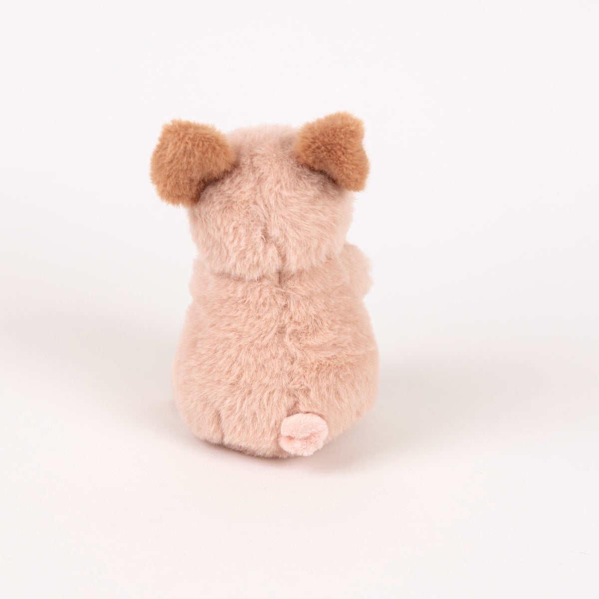 A small plush toy shaped like a pig, shown from the back on a clean white studio background. The toy has soft, fuzzy light pink fur, darker brown ears, and a small pink snout.