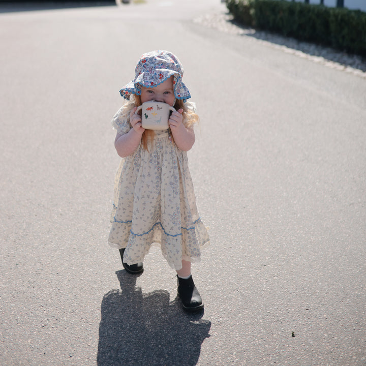 Young girl in a dress and hat holding a cup on a road