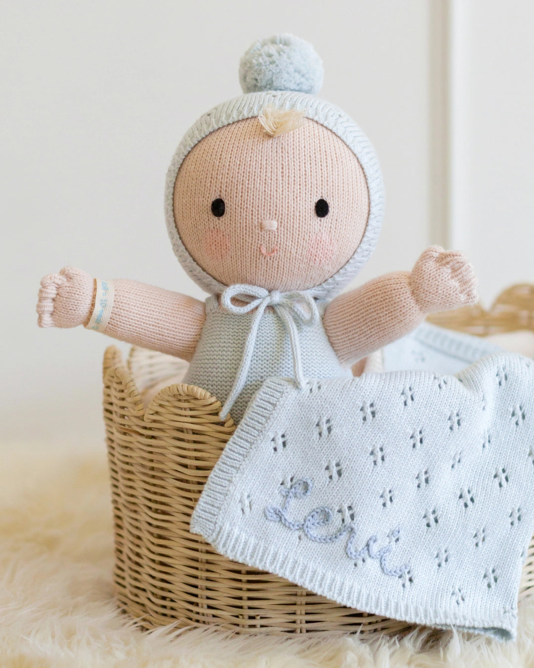 Knitted baby doll with a blanket in a basket on a soft surface