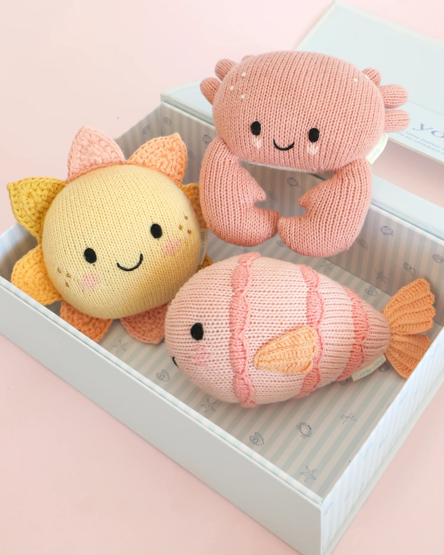 Three knitted toys shaped like a sun, a crab, and a fish on a pink surface.
