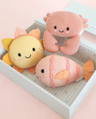Three knitted toys shaped like a sun, a crab, and a fish on a pink surface.