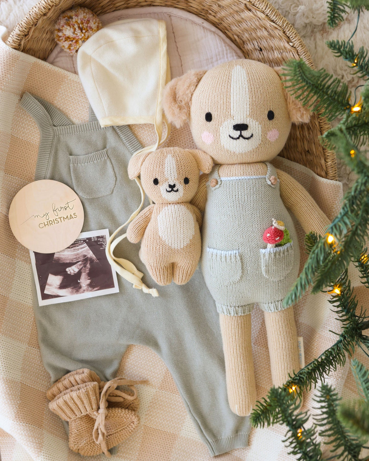 Knitted bear toy with overalls, baby booties, and photo on a textured surface with Christmas decorations.