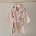 Pink children's robe with bear ears on a hanger against a beige wall.