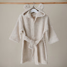 Beige children's robe with bear ears on a hanger against a beige wall