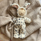 Plush toy resembling a baby in a bunny costume on a textured beige blanket