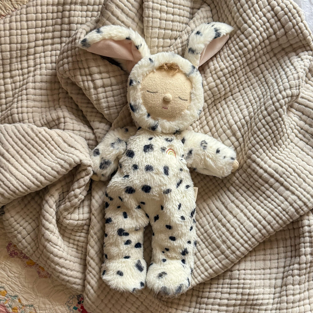 Plush toy resembling a baby in a bunny costume on a textured beige blanket