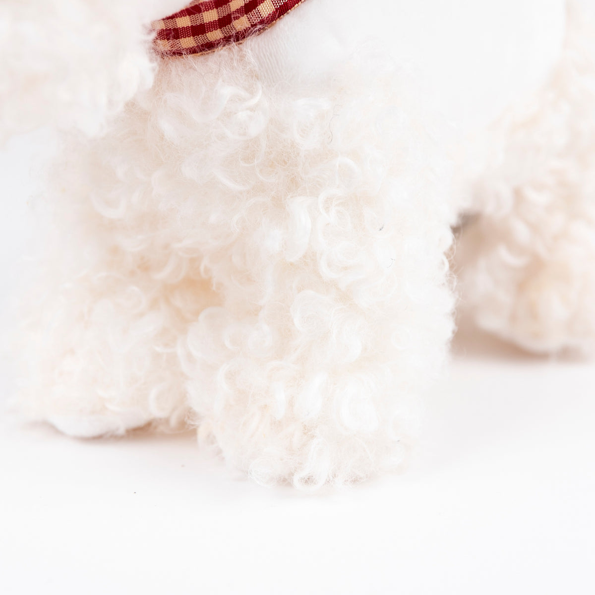 Close-up of a fluffy white dog with a red and white checkered bow tie on a light background