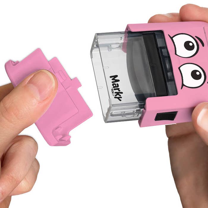 Pink Markr by OOLY stamp with cartoon face held by a hand on a white background