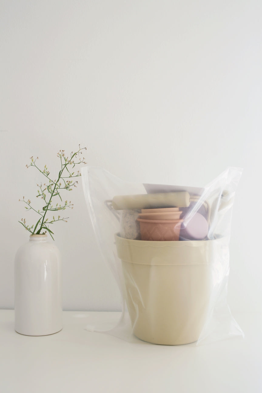 Beige basket with a pink item, white vase with greenery on a light background