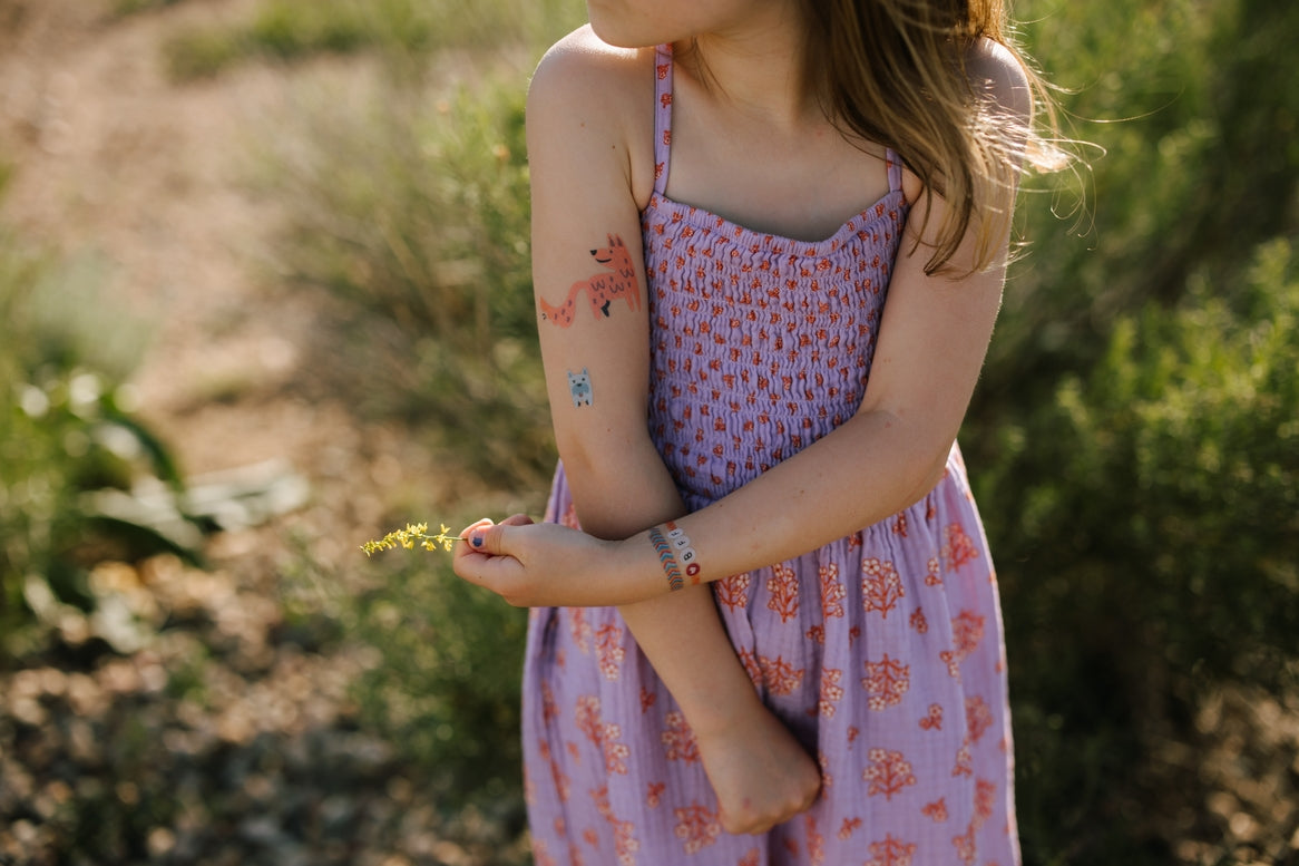 Child in a pink floral dress standing outdoors with a blurred natural background