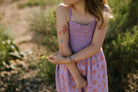 Child in a pink floral dress standing outdoors with a blurred natural background