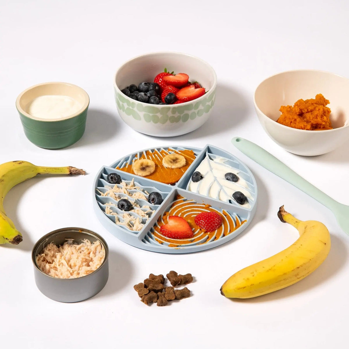 Assorted food items including bowls of fruit, a plate with divided sections, and bananas on a white background.
