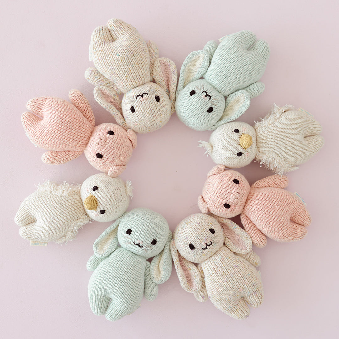 Set of soft, pastel-colored bunny toys arranged in a circular pattern on a pink background.