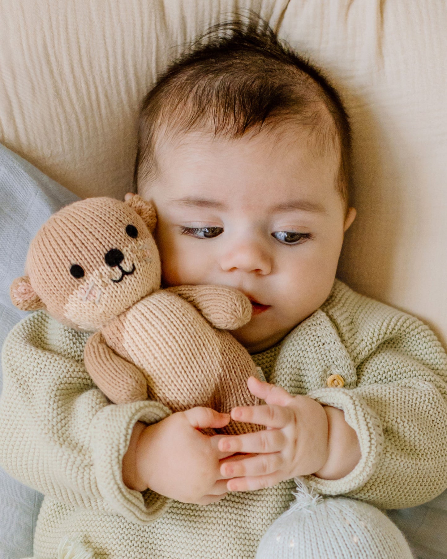 Baby holding a knitted teddy bear on a soft surface