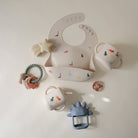 Collection of baby accessories including bib, teether, and cups on a white background