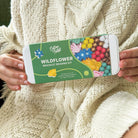 Person holding a Wildflower bracelet beading kit packaging against a beige knitted background