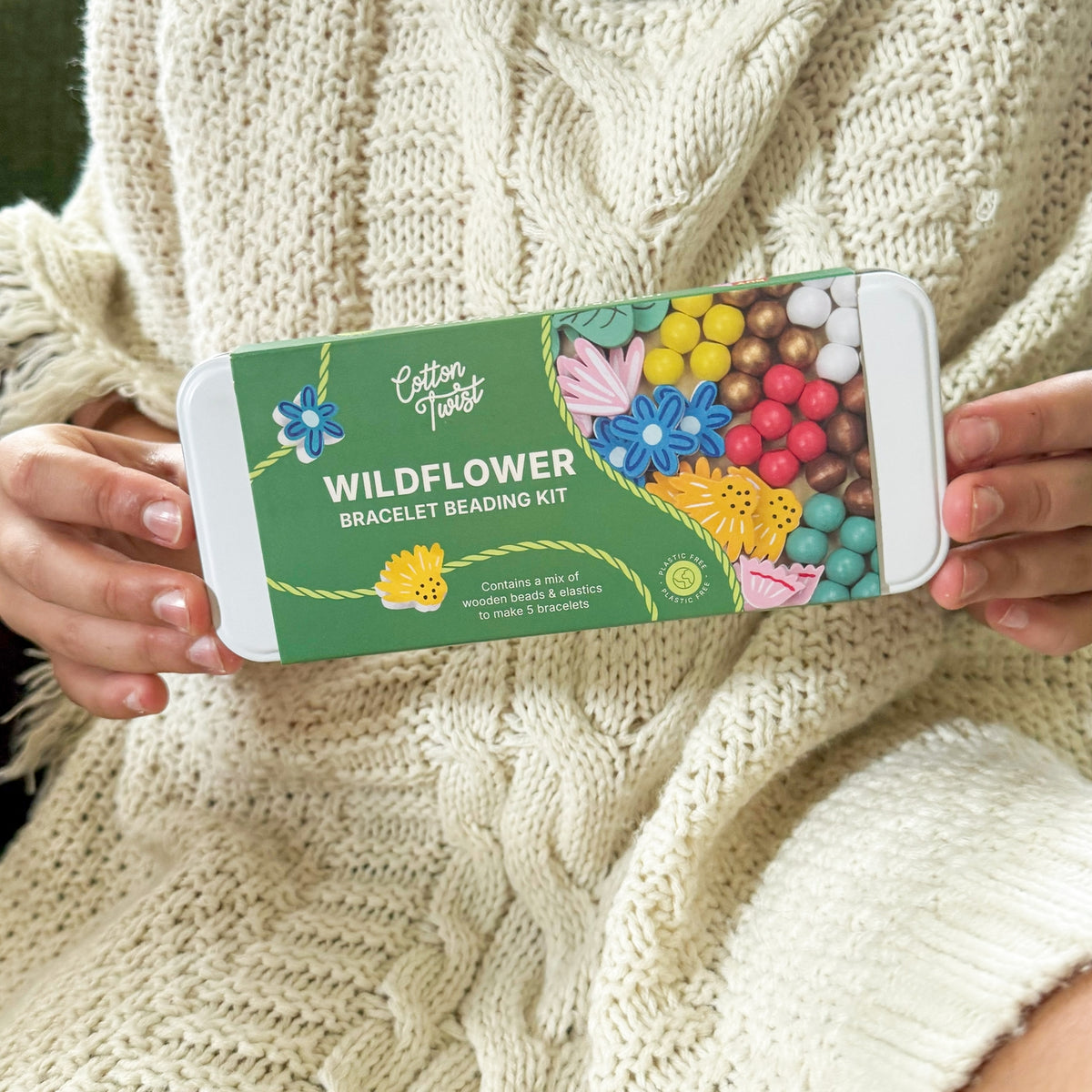 Person holding a Wildflower bracelet beading kit packaging against a beige knitted background