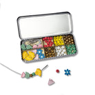 Jewelry-making kit with beads and tools in a metal tin on a white background