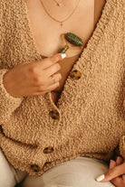 Person wearing a beige cardigan with a button detail, holding a green object.