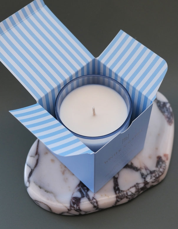 White candle in a blue striped box on a marble surface