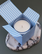 White candle in a blue striped box on a marble surface