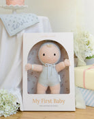 A knitted baby doll with a pale peach face and limbs, wearing a light blue knit bonnet with a pom-pom and a matching blue knitted romper.