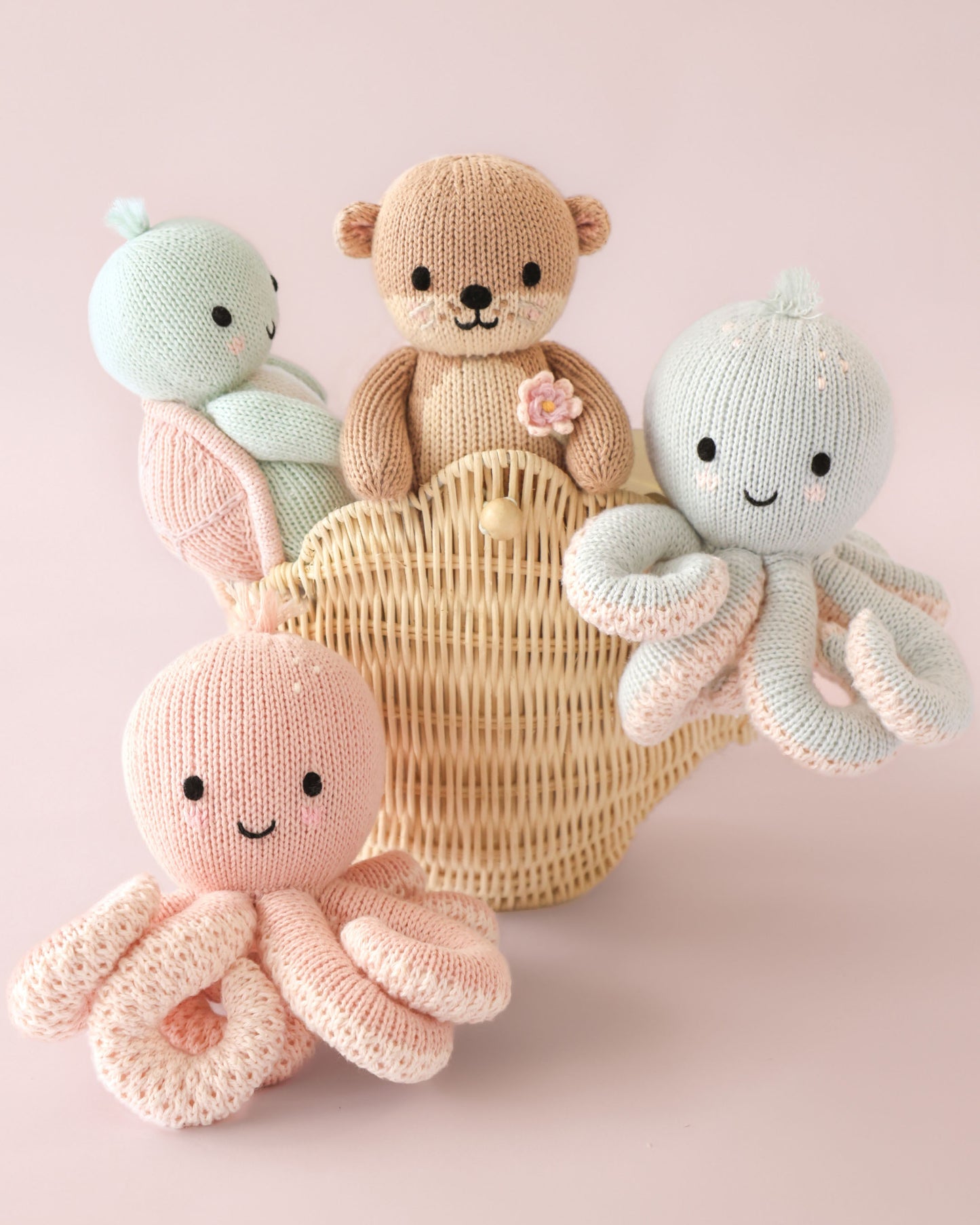 Knitted toys including a bear, octopus, and snake in a basket on a pink background