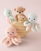 Knitted toys including a bear, octopus, and snake in a basket on a pink background