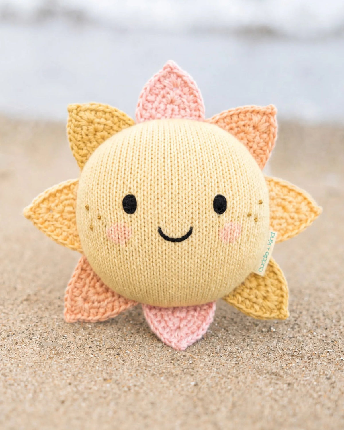Knitted sunflower plush toy on sand background